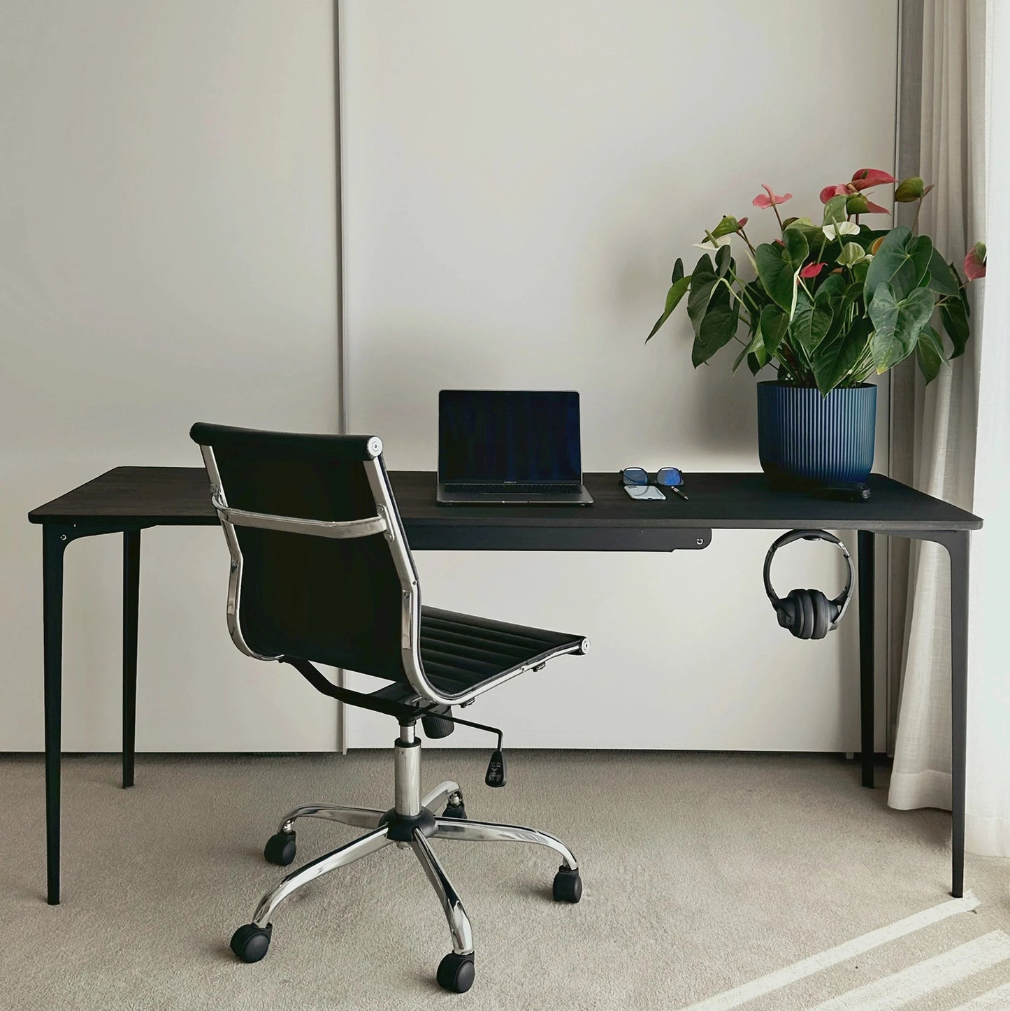 black modern office desk with chair, laptop, and plants in a minimalistic room.