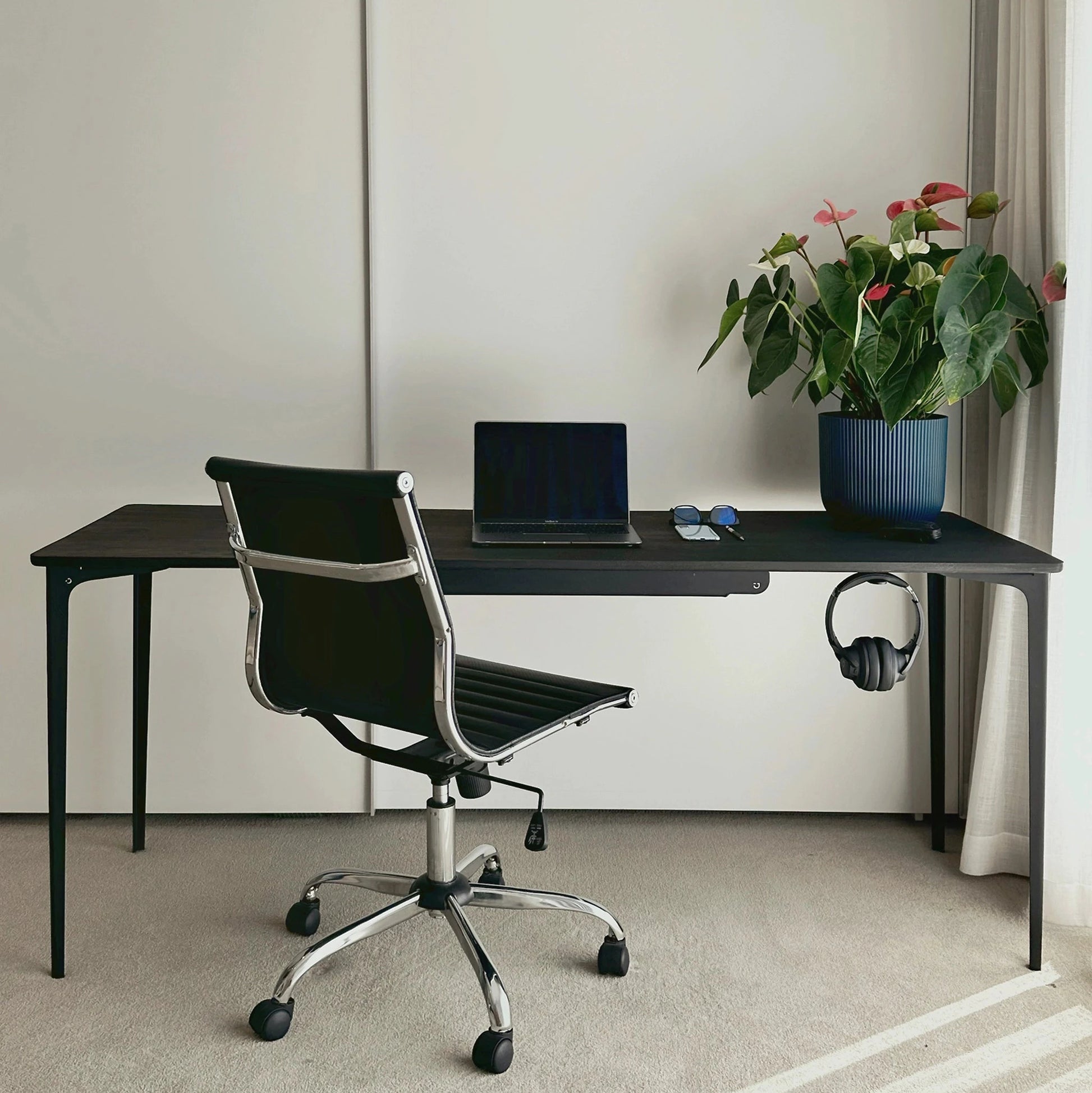 black modern office desk with chair, laptop, and plants in a minimalistic room.